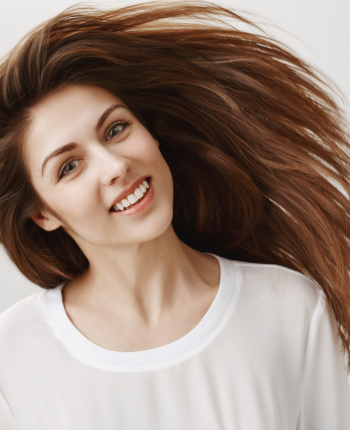 Happy people are beautiful. Portrait of attractive young caucasian brunette waving head and smiling broadly, being satisfied with shampoo that straighten hair strands, standing over gray background